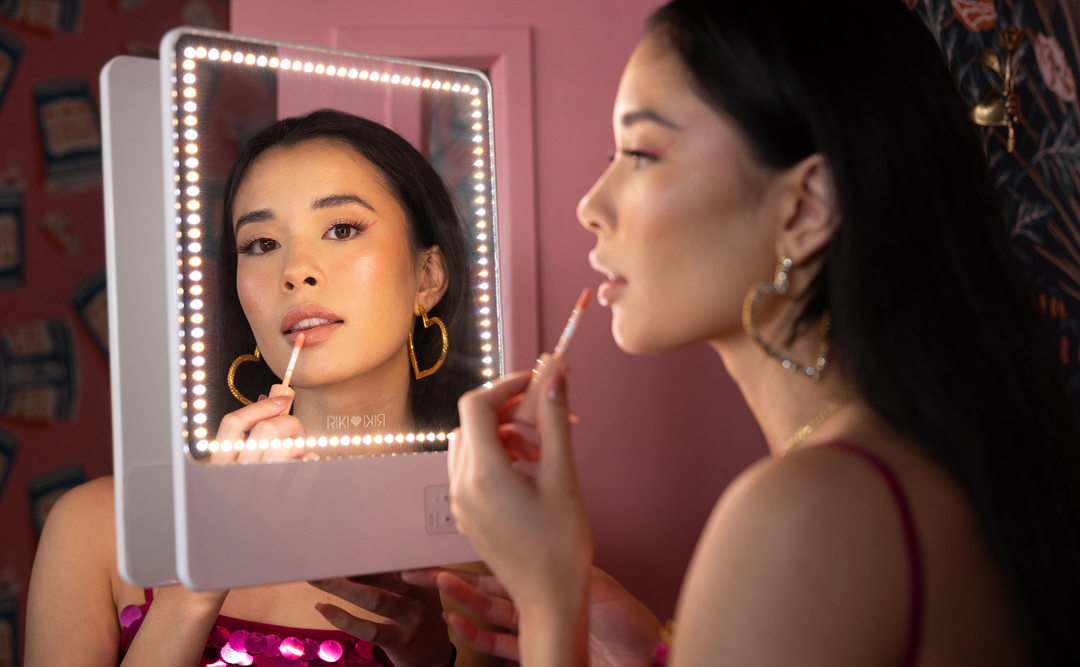 Female model applying makeup with RIKI SKINNY DUO attached to bathroom mirror in adjustable warm and cool lighting.